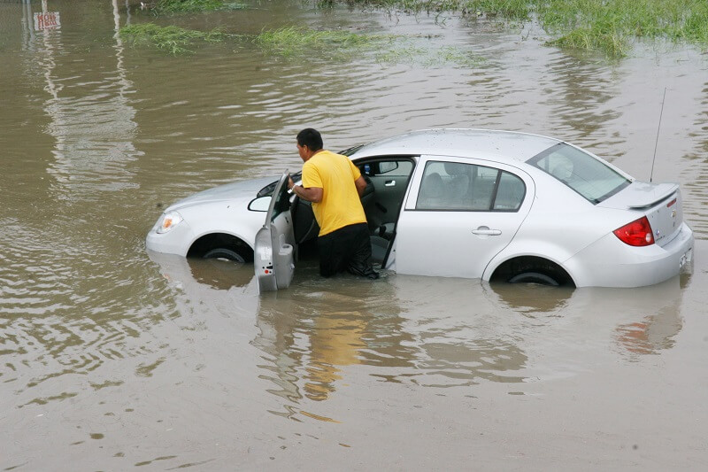 man pushing his car through flood waters