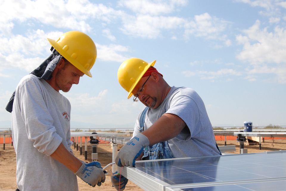 two men in yellow hard hats working on a solar panel